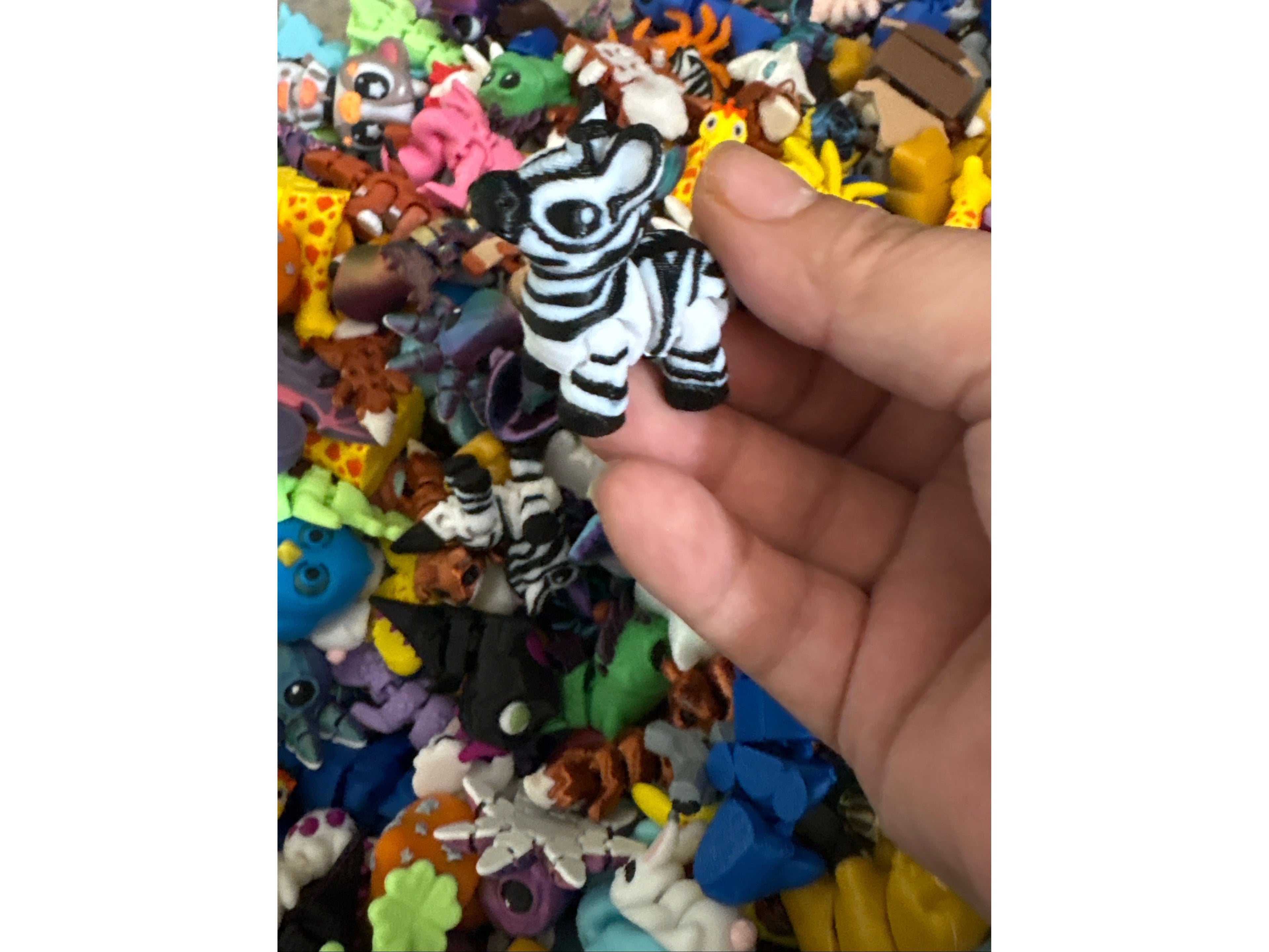 Hand holding a zebra figurine over a collection of colorful animal figurines.