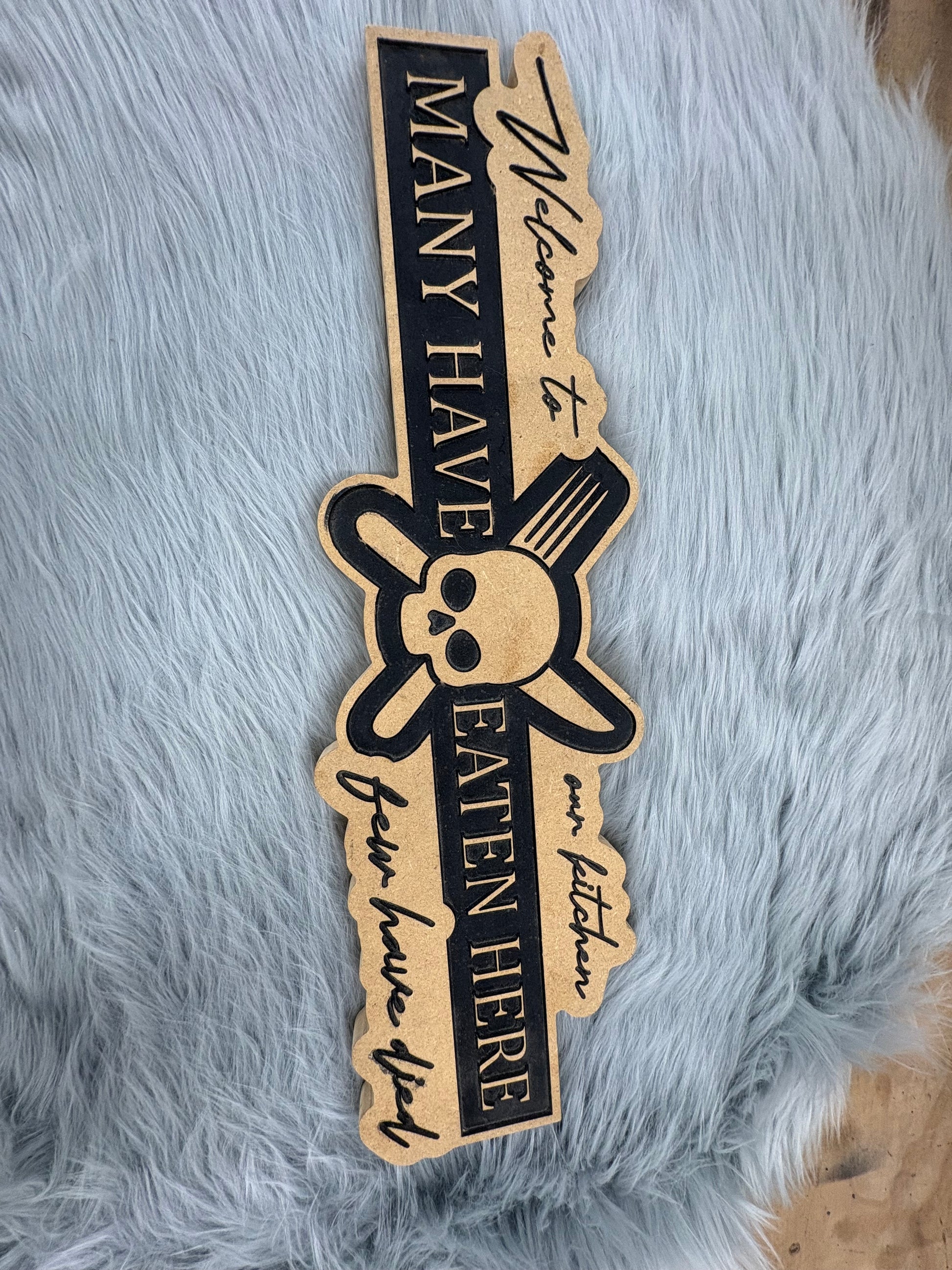 CNC Engraved Kitchen Sign – “Welcome to Our Kitchen: Many Have Eaten Here, Few Have Died” with Skull & Crossbones | Rustic Black & Wood Look | 9.5” x 16” | $30